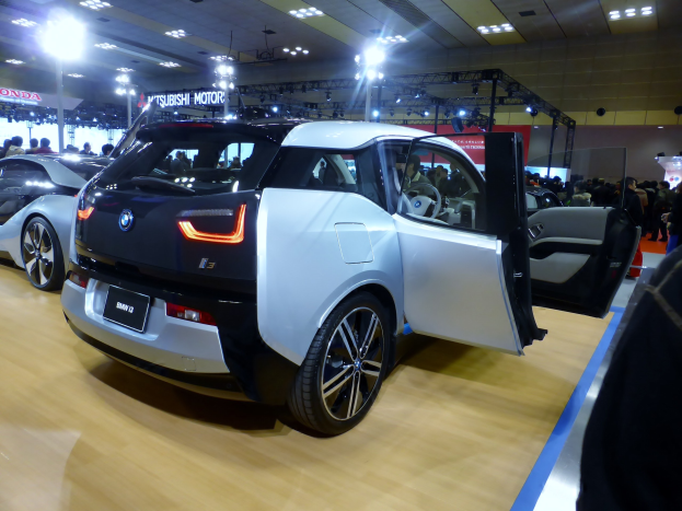 Ein weißer und schwarzer BMW i3 Elektroauto auf der IAA in Frankfurt, umgeben von Menschen, mit beleuchteter Decke und Informationsschildern im Hintergrund.
