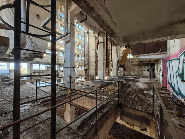 Verlassenes Gebäudeinnere mit Graffiti-beschmierten Wänden, bröckelnden Strukturen, Geländern, Pfählen, Rohren und zerbrochenen Fenstern, mit einem Wasserzeichen unten.