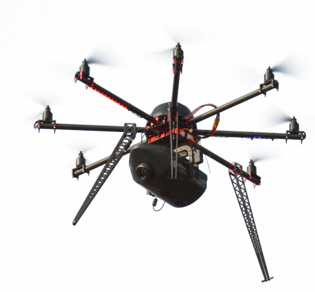 Eine schwarze Drohne mit Kamera fliegt durch die Luft vor einem weißen Hintergrund.