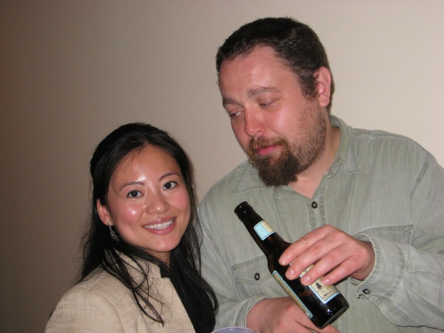 Ein Mann mit einer Flasche schaut eine lachende Frau an einer Wand im Hintergrund an.