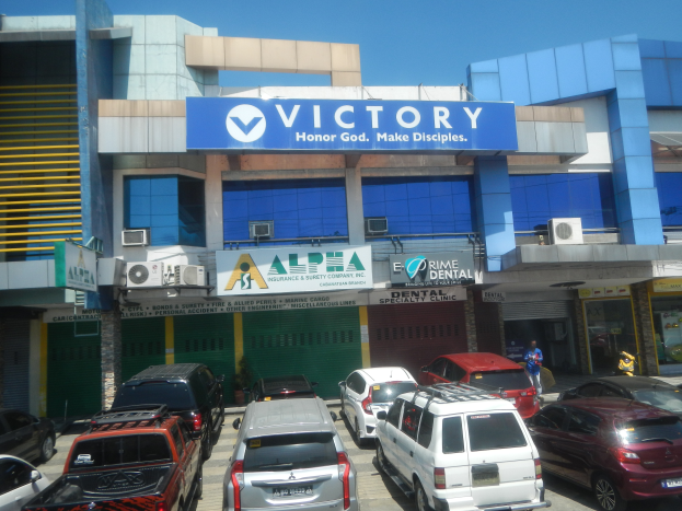 Gebäude der Victory Dental Clinic in Cebu City, Philippinen, mit Fahrzeugen auf der Straße, einer Person in der Nähe und sichtbaren Texttafeln.