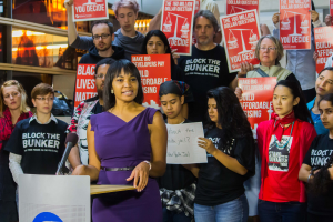 Eine Black-Lives-Matter-Aktivistin spricht an einem Podium mit Mikrofon vor einer Menge mit Schildern, mit Lichtern und Gegenständen im Hintergrund.