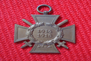 Ein rotes Tuch mit einer silbernen Medaille, die ein Lorbeerkranz ziert, mittig auf dem Tuch platziert mit eingravierter Inschrift, wahrscheinlich eine Ehrenmedaille.