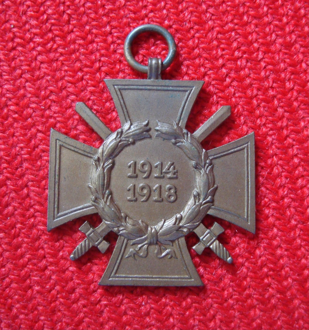 Ein rotes Tuch mit einer silbernen Medaille, die ein Lorbeerkranz ziert, mittig auf dem Tuch platziert mit eingravierter Inschrift, wahrscheinlich eine Ehrenmedaille.