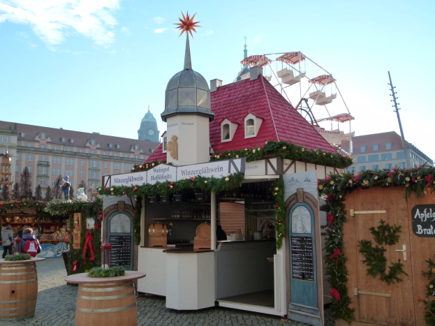 Ein kleines Gebäude mit rotem Dach und einem Riesenrad davor, umgeben von Menschen und Festdekorationen bei einem Outdoor-Event.