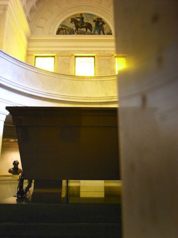 Das Innere eines Gebäudes mit einer Statue auf der linken Seite, einer Wand mit Glasfenstern und einem Gemälde an der Decke.