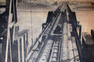 Ein Schwarz-Weiß-Foto einer Bahnschiene mit einer Brücke im Hintergrund, umgeben von Werkzeugen und Materialien.