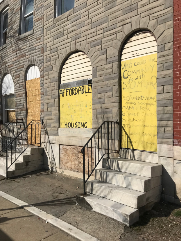 Verschlossenes Gebäude mit einer Tafel, die "Bezahlbarer Wohnraum" lautet, Treppe mit Geländern, die zur Einfahrt führen, und eine Straße unten.