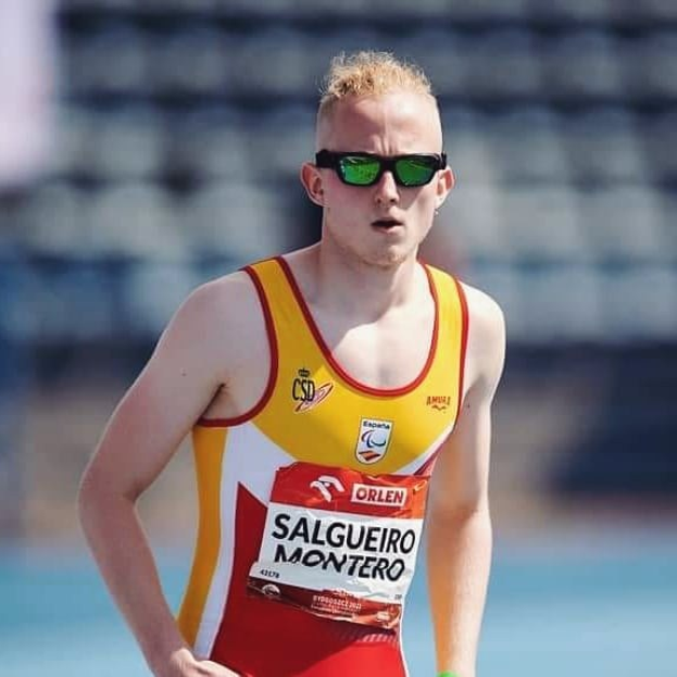 Ein Triathlet in Anzug und Sonnenbrille steht auf einer Bahn mitten im Rennen, die Arme verschränkt mit einem entschlossenen Gesichtsausdruck.