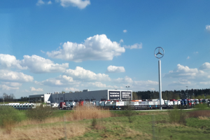 Mercedes-Benz-Fabrik in Deutschland mit Fahrzeugen auf der Straße, umgeben von Grünflächen und Gebäuden unter einem bewölktem Himmel.