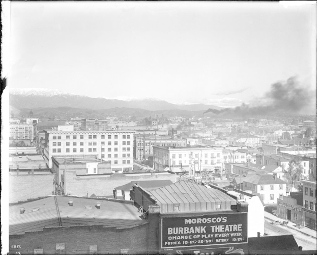Ein Schwarz-Weiß-Bild einer Fabrik mit Rauch, der aus ihrem Schornstein aufsteigt, umgeben von Gebäuden.