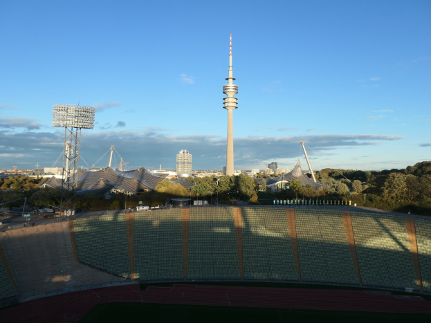 Olympiastadion in Berlin, Deutschland, mit dem TV-Turm im Hintergrund, umgeben von Bäumen, Gebäuden und Lichtern unter einem bewölktem Himmel.