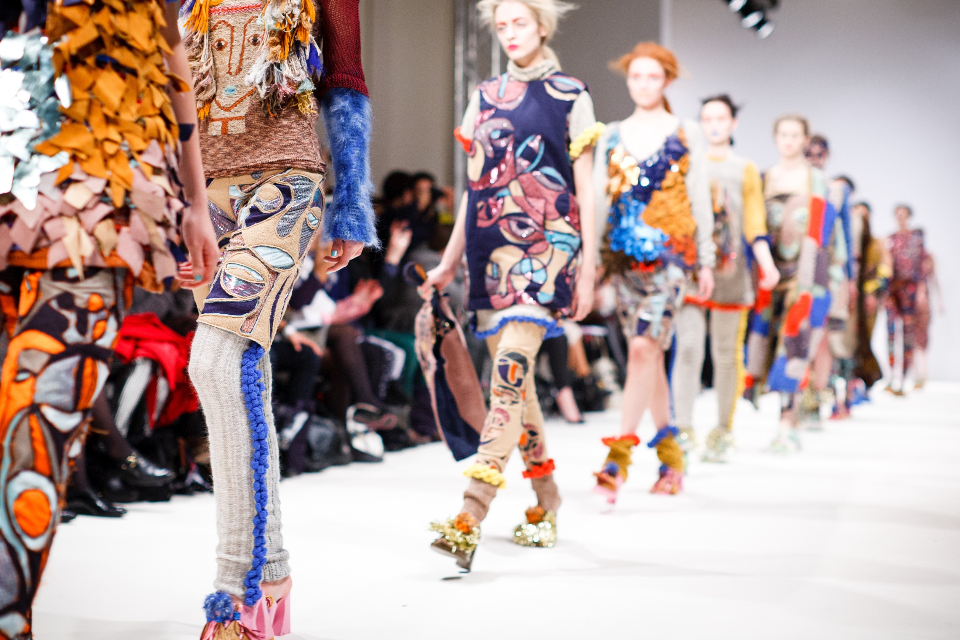 Eine Gruppe Von Frauen, Die Eine Laufsteg In London Fashion Week Heruntergehen, Mit Einer Zuschauerschaft Im Hintergrund Unter Helligen Lichtern, Schaffend Ein Etwas Verwischtes, Traumhaftes Effekt.