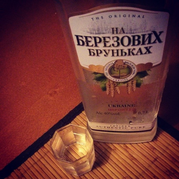 Ein klares Glas mit einer goldenen Flüssigkeit, wahrscheinlich Alkohol, das auf einer dunklen Unterlage steht.