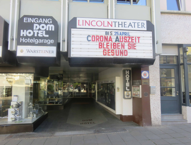 Das Lincoln Theater in Berlin, Deutschland - ein Gebäude mit Glasfenstern und -türen sowie einer Tafel mit Text, die verschiedene Objekte im Inneren zeigt und so den Eindruck einer pulsierenden Stadtkulisse vermittelt.