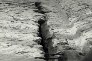 Schwarzes und weiße Foto eines großen Risses in einer Bodenleitung mit einem Wasserzeichen auf der linken Seite.