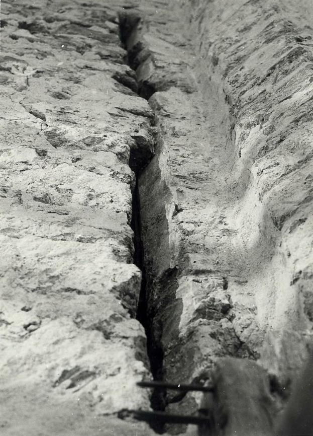 Schwarzes und weiße Foto eines großen Risses in einer Bodenleitung mit einem Wasserzeichen auf der linken Seite.