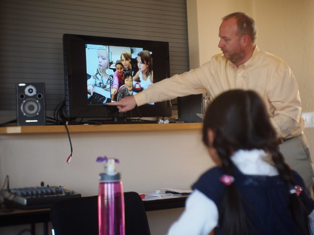 Ein Mann und ein Kind befinden sich in einem Raum mit einem Fernseher, einem Lautsprecher und einer Musikanlage; der Mann erklärt etwas aus dem Fernsehen, und es gibt eine Flasche links neben dem Kind.