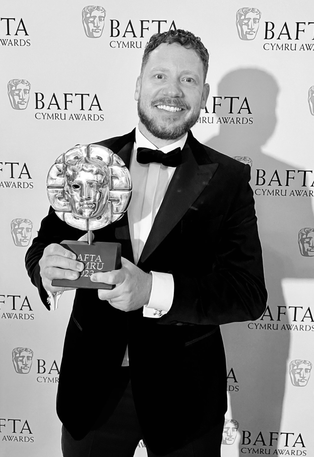 Ein Mann in einem Smoking, der eine BAFTA-Trophäe hält und lächelt, mit einem Hintergrundschild mit der Aufschrift "BAFTA Awards 2018."