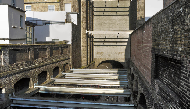 Ein Zug fährt aus einem Tunnel zwischen Gebäuden heraus.