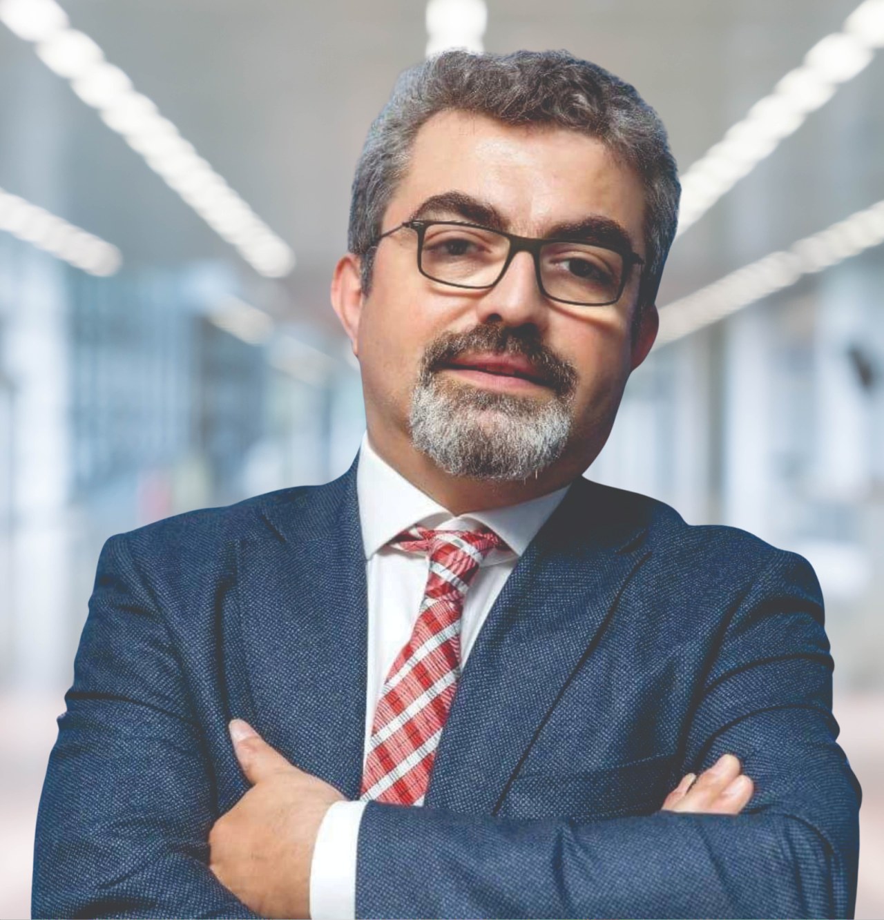 Ein Mann im Anzug und Krawatte mit verschränkten Armen und Brille steht vor einem unscharfen Hintergrund mit Text, der ihn als neu ernannten Marketingchef identifiziert.