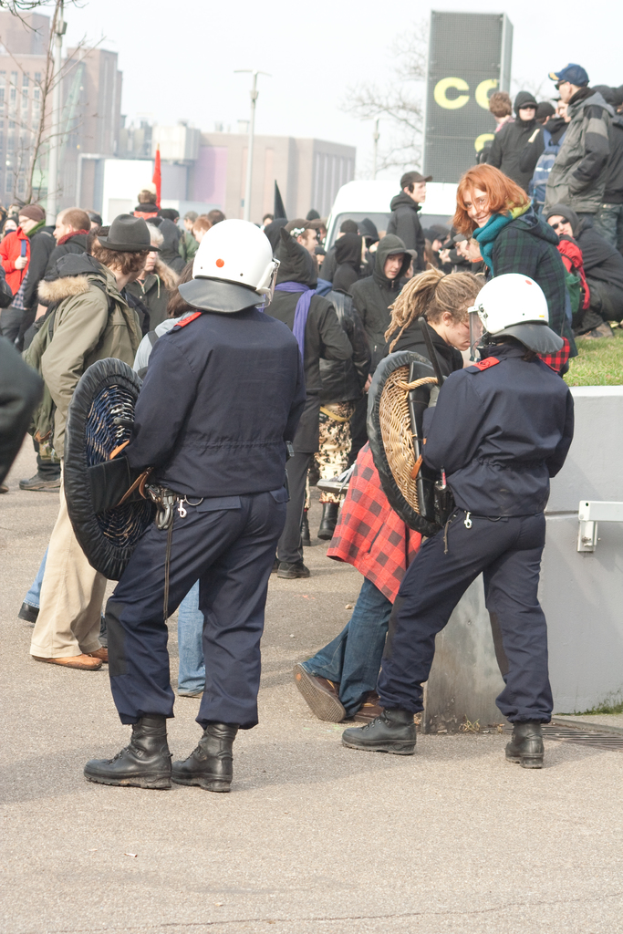 Eine Gruppe von Menschen, die auf einer Straße mit zwei Polizisten vorne, Gebäuden im Hintergrund und Boden unten gehen.