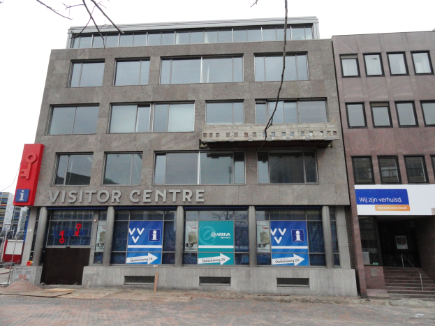 Großes Gebäude mit einer "Besucherzentrum"-Schilder, umgeben von anderen Gebäuden, Bäumen und einem klaren blauen Himmel.