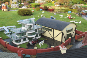 Ein detailliertes Modell einer Kleinstadt mit zahlreichen Gebäuden, Bäumen, Fahrzeugen, Flugzeugen, Menschen und anderen Objekten, mit Häusern am Boden, die einen belebten Eindruck einer Stadt erwecken.