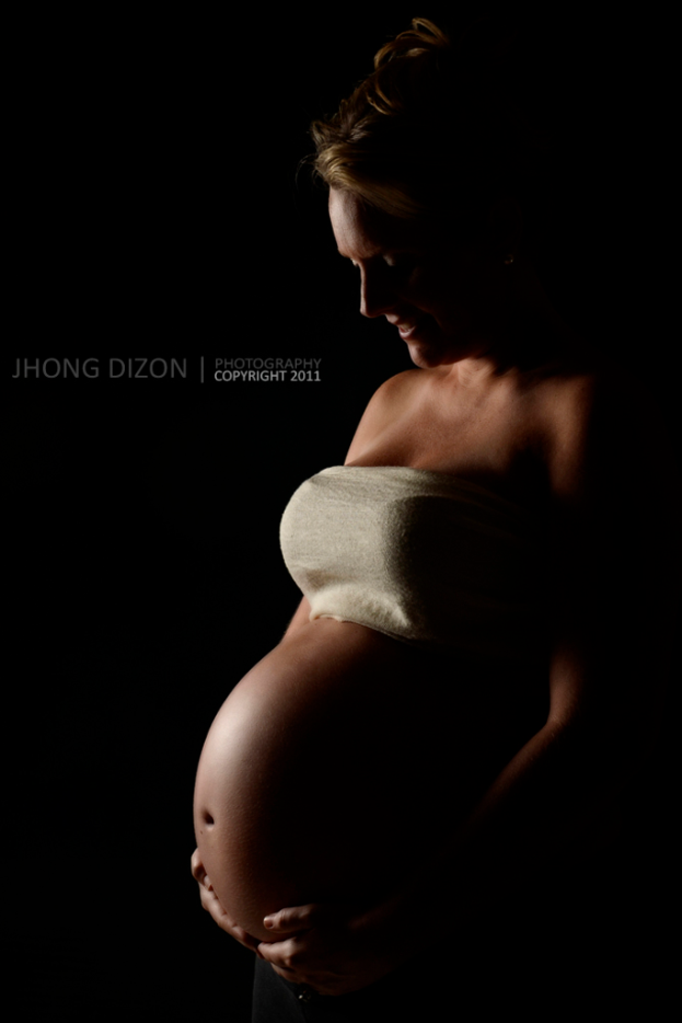 Eine Frau lächelt, während sie ihren Bauch mit beiden Händen berührt.