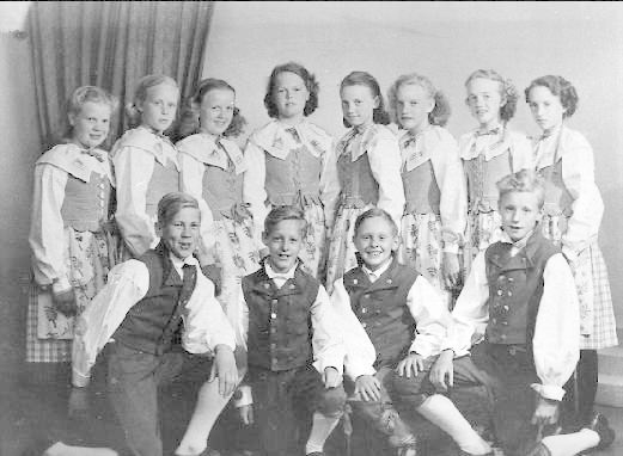 Schwarzes und weißes Foto von Kindern, die vor einer Vorhangwand mit dem Text "1930er-Kinder-Schule" unten posieren