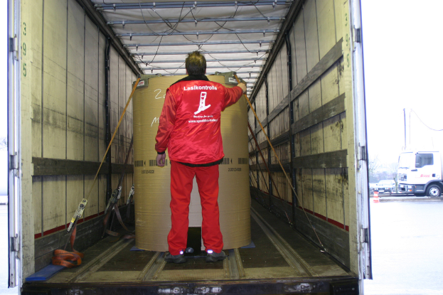 Eine Person hält eine Trommel in einem Lkw, mit mehreren Fahrzeugen auf der Straße draußen.