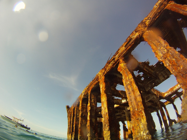 Ein Schiff befindet sich auf dem Wasser im unteren linken Bildrand, mit einem hölzernen Dock auf der rechten Seite.