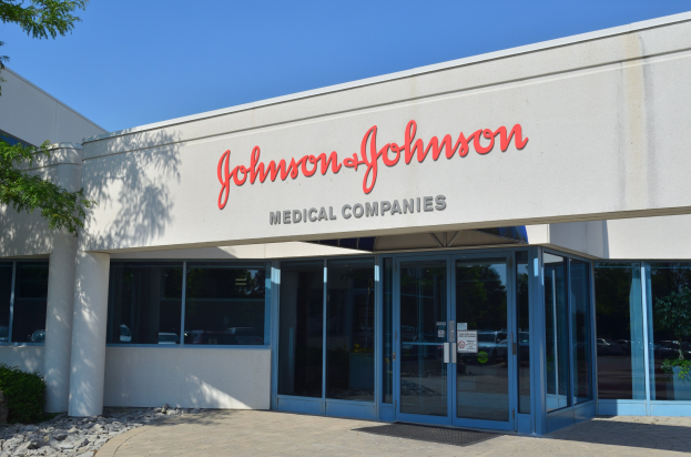 Außenansicht des Johnson & Johnson Medical Companies-Gebäudes mit Glaswänden, Text an der Fassade, Landschaftsgestaltung einschließlich Steinen und Pflanzen, einem Baum auf der linken Seite und einem klaren blauen Himmel im Hintergrund.