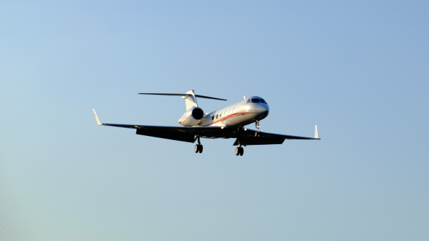 Ein Privatjet mit ausgefahrenem Fahrwerk gleitet durch einen hellblauen Himmel.