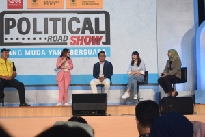 Eine Gruppe von Menschen sitzt auf einer Bühne mit einer Frau in der Mitte, die ein Mikrofon hält, einer Zuschauermenge im Vordergrund und einem Banner mit der Aufschrift "Politischer Straßenkampf 2019" im Hintergrund.