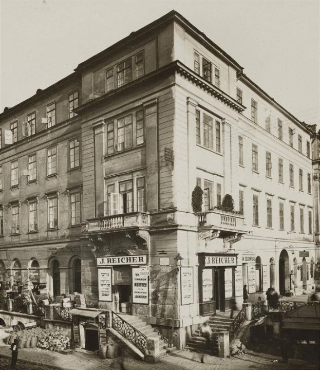 Das J Reicher Hotel in Berlin, ein altes Gebäude mit mehreren Fenstern, Treppen mit Geländern und Töpfen mit Pflanzen, mit einigen Menschen und einem sichtbaren Himmel im Hintergrund.