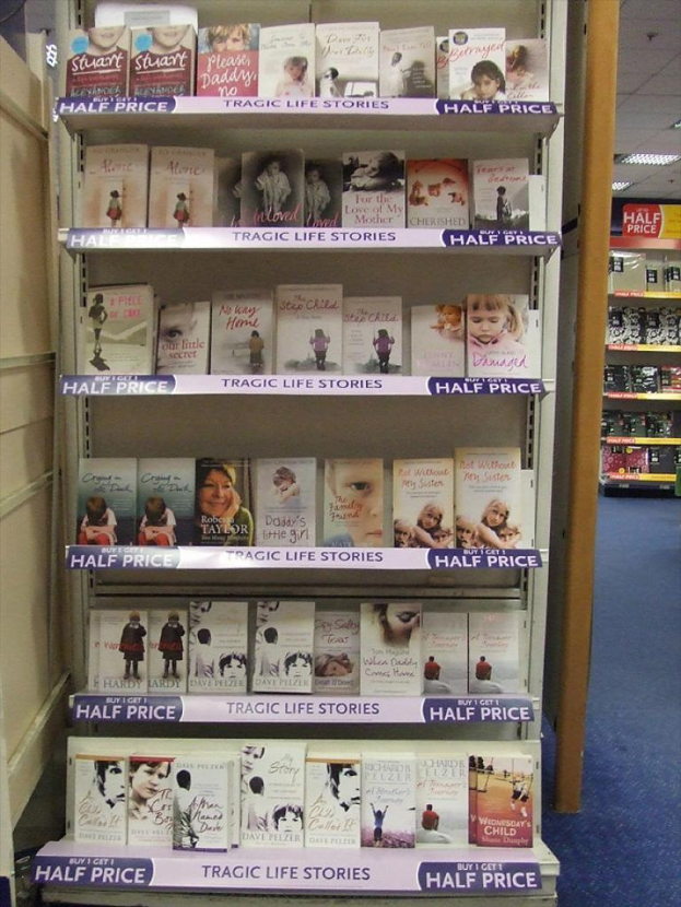 Eine Innenansicht, die ein Bücherregal zeigt, das mit vielen Büchern gefüllt ist, eine Tür auf der linken Seite, ein zweites Regal im Hintergrund mit ein paar Gegenständen und Lampen oben.