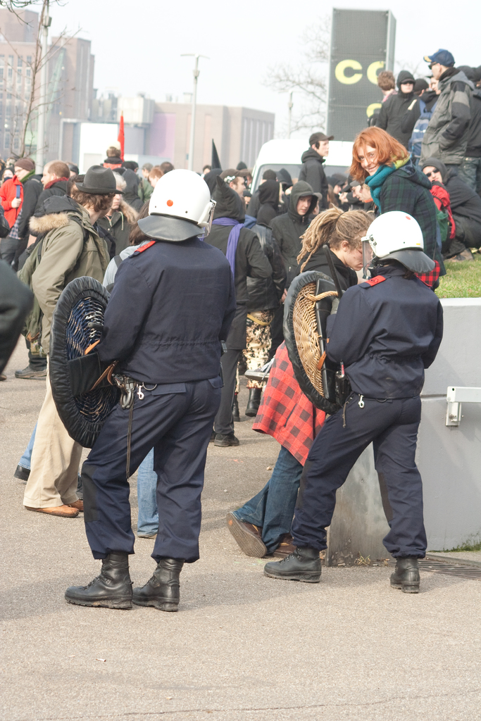 Eine Gruppe von Menschen, die auf einer Straße gehen, mit zwei Personen in der Vordere, die wie Polizei aussehen, Gebäude im Hintergrund und Boden unten.