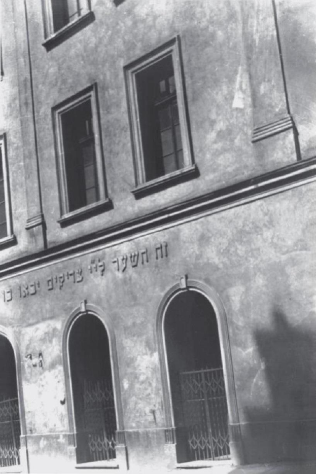 Ein Schwarz-Weiß-Foto eines historischen Gebäudes in Jerusalem, das mutmaßlich eine Synagoge ist, mit Fenstern, Türen und einem Metallzaun.