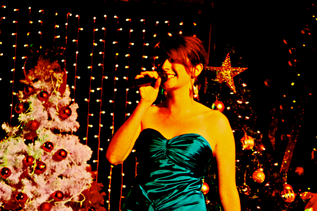 Eine Frau steht mit einem Mikrofon in der Hand vor Weihnachtsbäumen und Lichtern