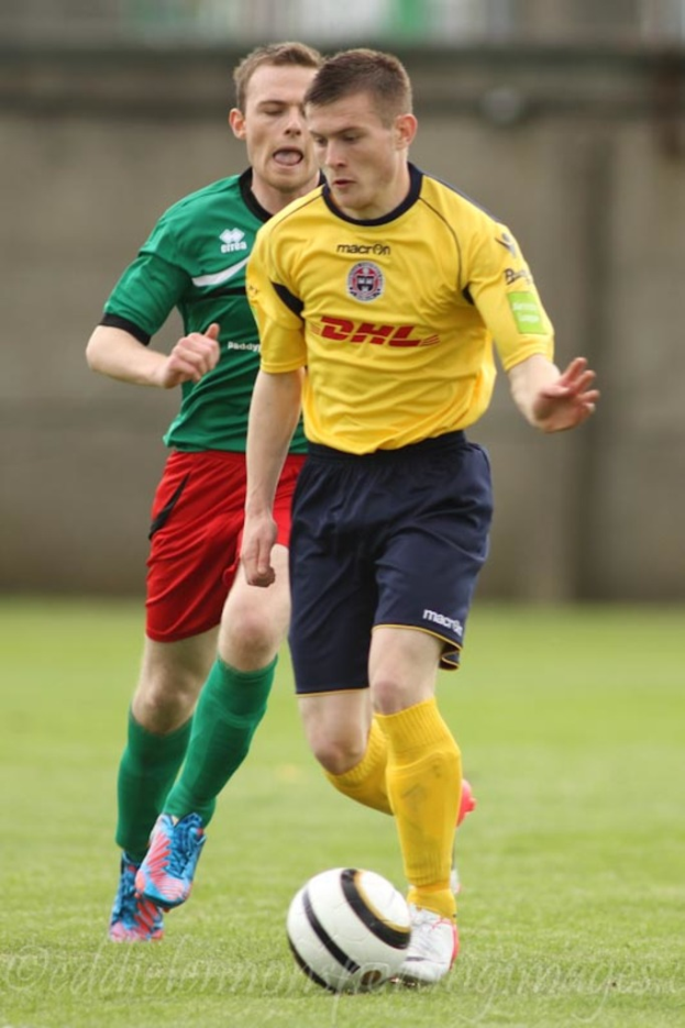 Zwei Männer spielen Fußball auf einem grünen Feld mit einem Ball, mit einem unscharfen Hintergrund und Text unten.