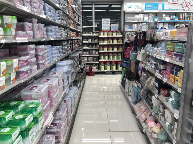 Ein unordentlicher chinesischer Supermarktgang mit Regalen voller Kartons, Flaschen, Taschen und anderen Produkten, beleuchtet von Deckenlampen, mit Schildern in chinesischer Schrift, einem montierten Feuerlöscher und einem sichtbaren Grundriss.
