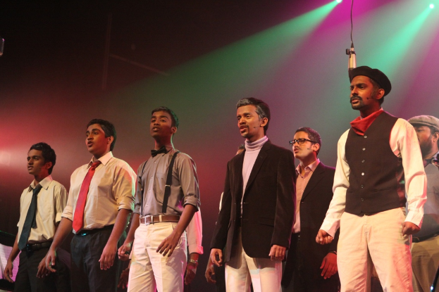 Eine Gruppe von Männern auf der Bühne, die ein Drama spielen, mit grünen Scheinwerfern im Hintergrund.