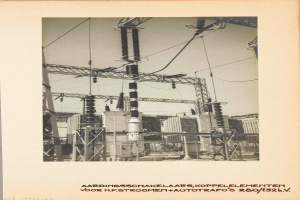 Ein altes Schwarz-Weiß-Foto einer elektrischen Umspannstation mit sichtbaren Transformatoren, Drähten und Text am unteren Rand.