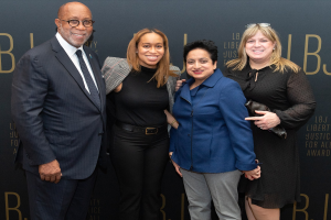 Vier Personen auf einem roten Teppich bei den "Liberty Justice for All Awards", die fröhlich in die Kamera lächeln.