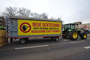 Ein Lastwagen mit einer Aufschrift auf der Rückseite fährt eine Straße in Deutschland entlang, umgeben von Menschen, Bäumen, Gebäuden und unter einem klaren blauen Himmel, wahrscheinlich Teil einer Demonstration.