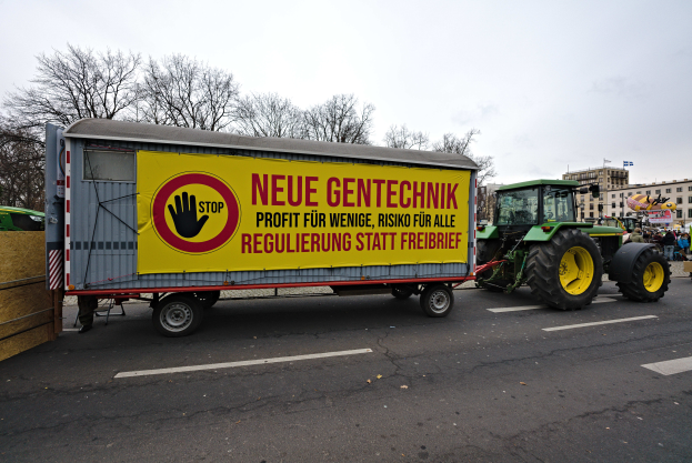 Ein Lastwagen mit einer Aufschrift auf der Rückseite fährt eine Straße in Deutschland entlang, umgeben von Menschen, Bäumen, Gebäuden und unter einem klaren blauen Himmel, wahrscheinlich Teil einer Demonstration.