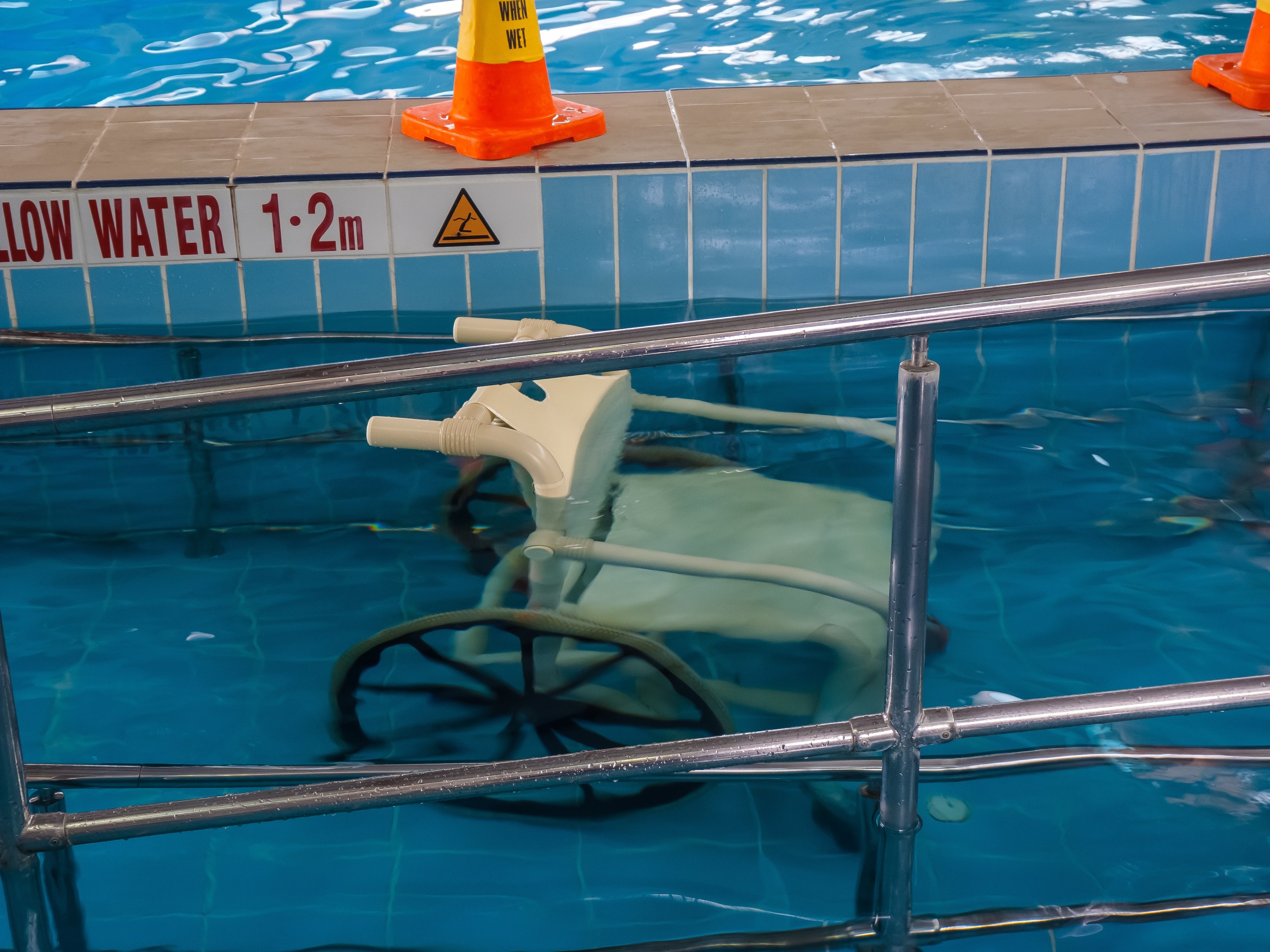 Schwimmbad mit einem Stuhl in der Mitte, umgeben von Sicherheitskegeln und einem Geländer und einem Schild an der Wand, das verfügbare Schwimmausrüstung anzeigt.
