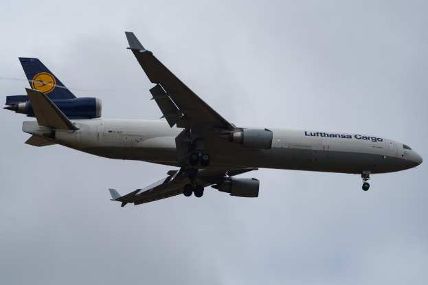 Ein Lufthansa Cargo Boeing 777-300ER im Flug, mit ausgefahrenen Flügeln und laufenden Triebwerken, mit sichtbarem Text auf dem Rumpf gegen einen wolkengefüllten Himmel.