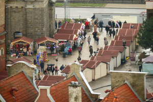 Eine belebte Stadtstraße mit Fußgängern, Gebäuden, Marktständen, einem Baum, einem Schild, einer Eisenbahnschiene und einem bewölkten Himmel.